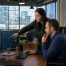Two IT professionals in a modern high-rise office discussing a cloud computing diagram on a computer monitor with city buildings in the background.