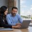 Two professionals collaborate on a laptop in a bright office overlooking the historic Collin County Courthouse in downtown McKinney, Texas.